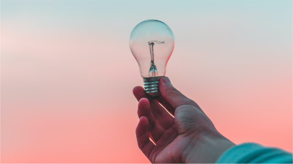 A hand holding an unlit incandescent light bulb up in the air