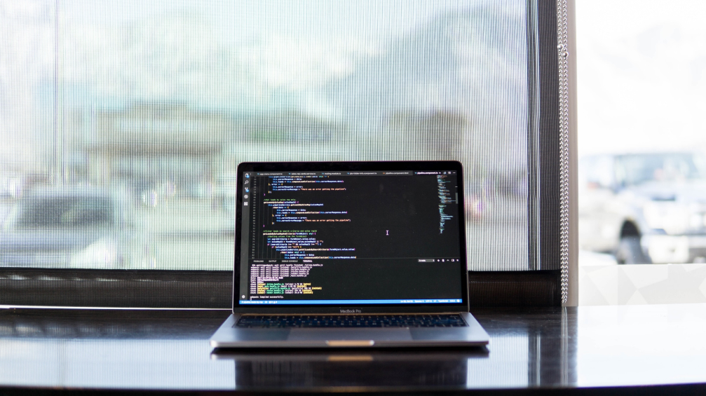 Photo of a laptop sitting on a desk with code displayed on its screen