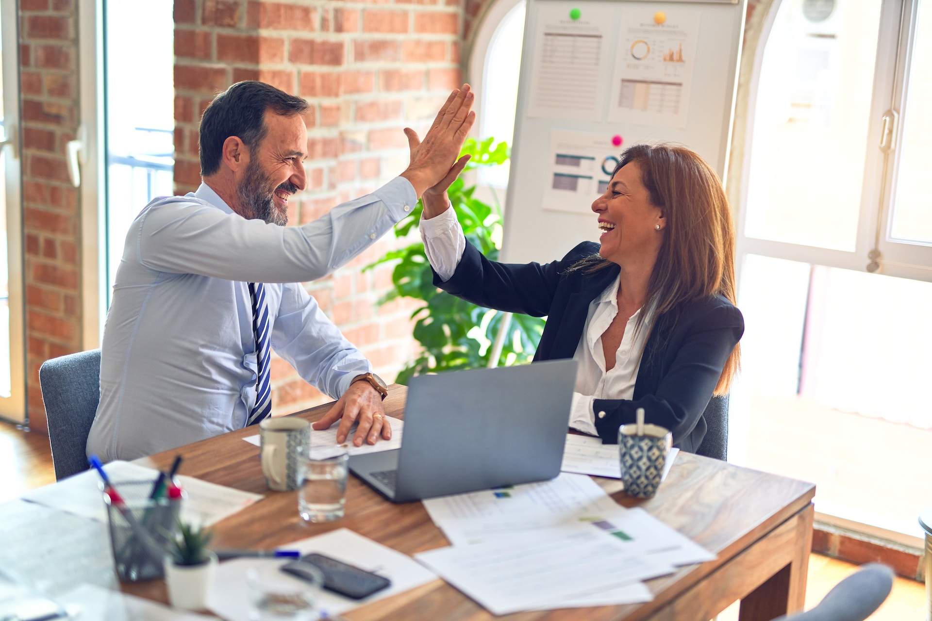 A man and a woman in a conference room setting, smiling and giving each other a high five
